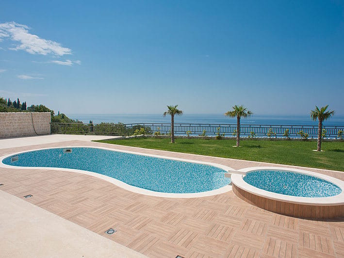 Piscine extérieure avec jacuzzi et vue sur la mer près de la villa à Reževići, Monténégro : terrasse carrelée et pelouse bien entretenue.