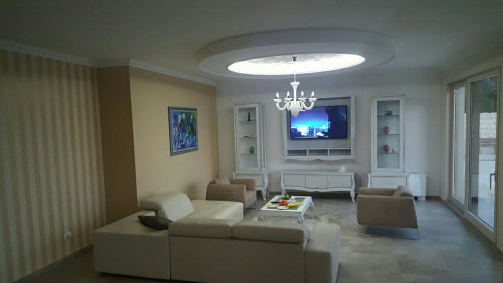 Salon spacieux avec mobilier blanc et plafond design dans une villa à Reževići, Monténégro.