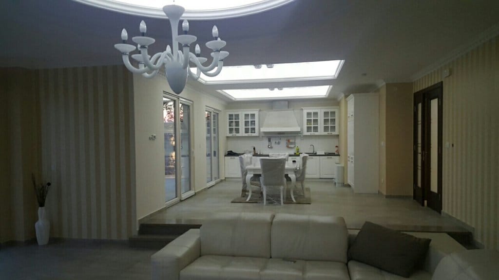 Salon spacieux avec mobilier blanc et cuisine dans une villa à Reževići, Monténégro : intérieur moderne avec lustre.