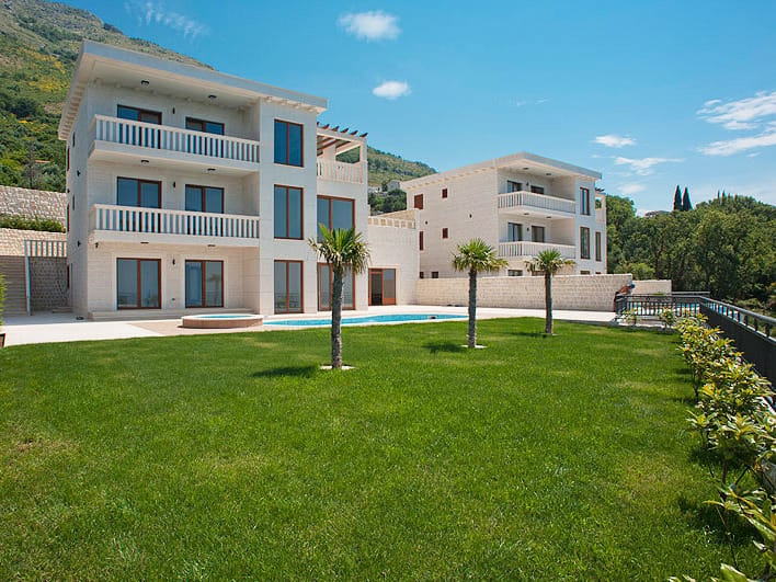 Villa moderne à Reževići, Monténégro : façade en pierre, terrasses, piscine et jardin bien entretenu avec les montagnes en arrière-plan.