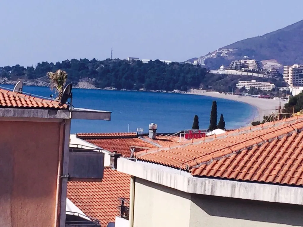 Vue sur la mer et la plage depuis un mini-hôtel à Rafailovici, Monténégro : toits en tuiles des maisons et panorama du littoral.