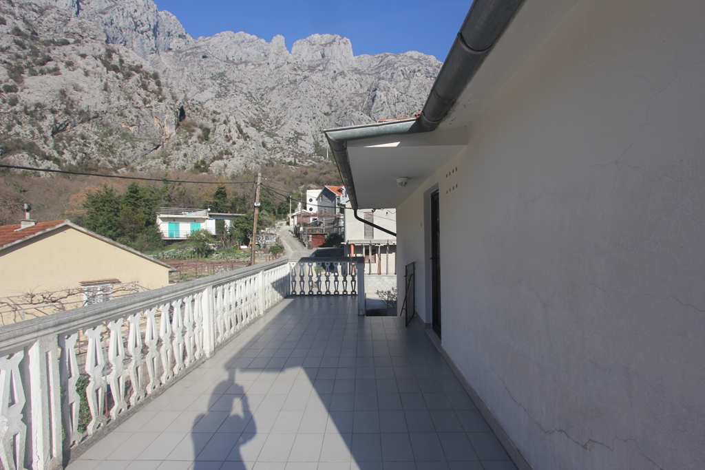 Przestronny balkon z balustradą i widokiem na góry w domu, Orahovac, Czarnogóra. Podłoga z płytek, jasne wykończenie elewacji.