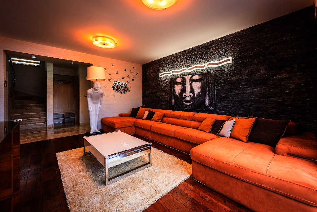 Wohnzimmer einer Villa in Krašići, Montenegro: oranges Ecksofa, Akzentwand aus Stein und Designer-Stehlampe.