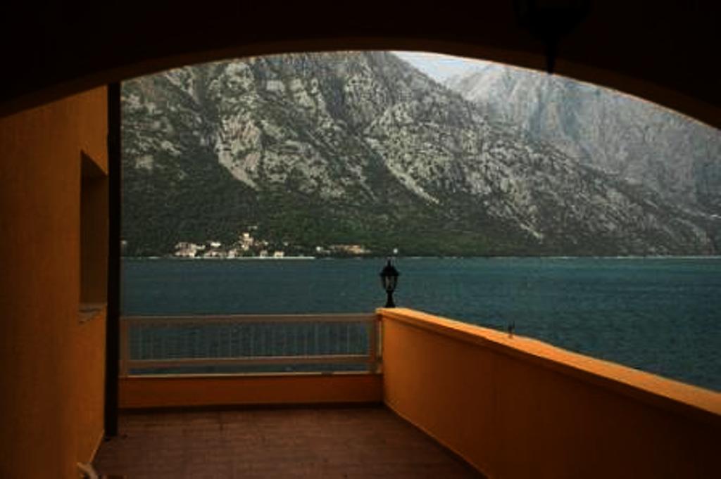 Pogled s balkona hotela u Stolivu, Crna Gora: panorama Bokokotorskog zaliva i planina, terasa sa žutim zidovima.