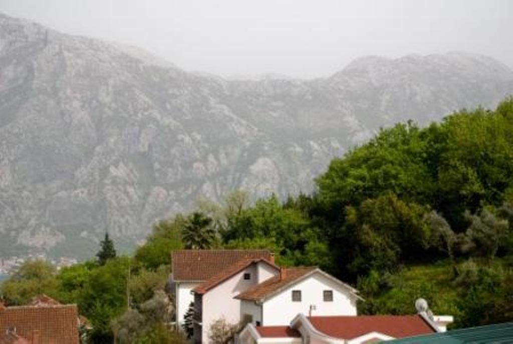 Pogled na planine i hotel u Stolivu, Crna Gora: bele zgrade sa krovovima od crepova među zelenilom i planinski pejzaž.