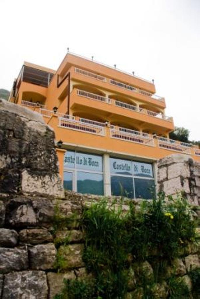 Fasada hotela Castello di Boca u Stolivu, Crna Gora: višespratna zgrada sa terasama i kamenim zidom kod ulaza.