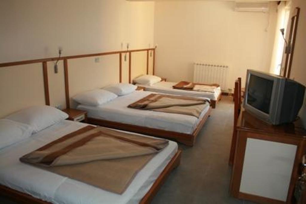 Trokrevetna soba u hotelu Stoliv, Crna Gora: tri kreveta sa belom posteljinom, drveni nameštaj i televizor.