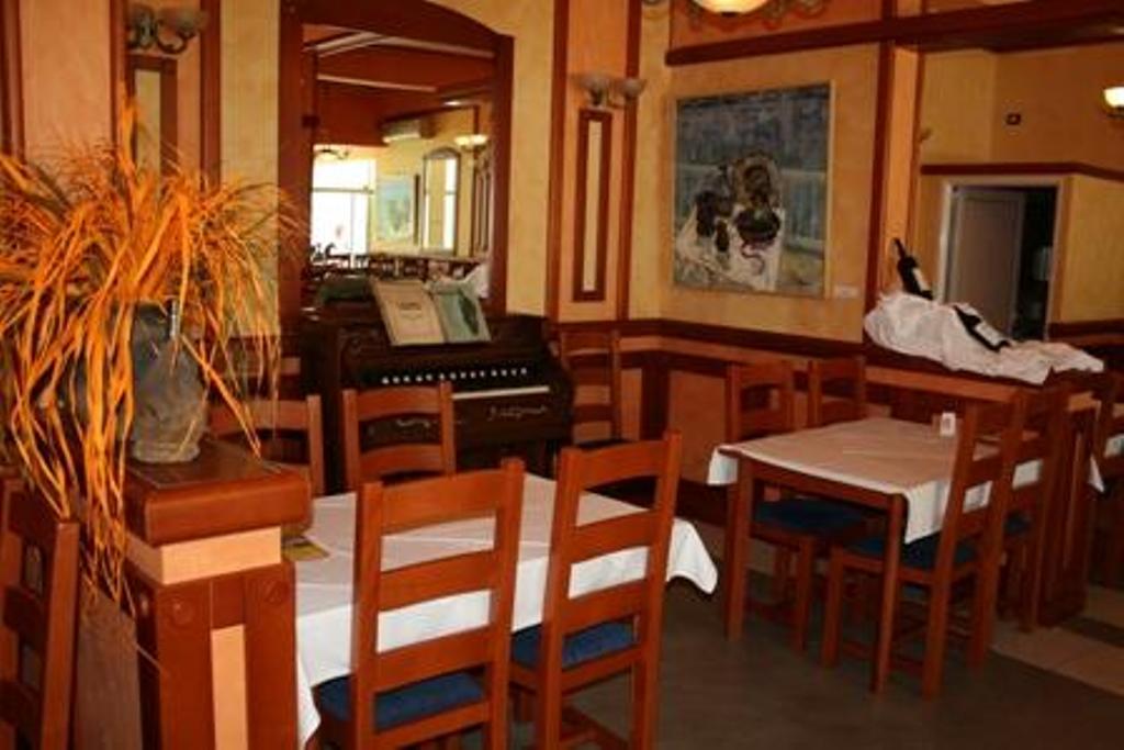 Enterijer restorana hotela u Stolivu, Crna Gora: drveni nameštaj, beli stolnjaci i starinski klavir u sali.