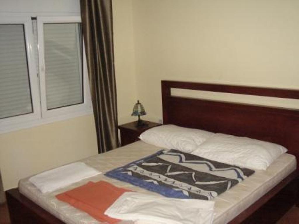 Spavaća soba sa bračnim krevetom u hotelu Stoliv, Crna Gora: tamni drveni nameštaj, svetli zidovi i prozor sa žaluzinama.