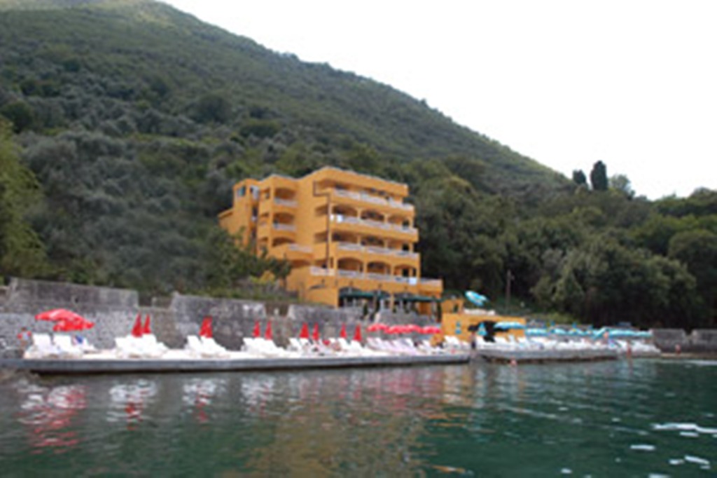 Žuti hotel sa terasama na obali mora u Stolivu, Crna Gora, sa sopstvenom plažom i ležaljkama.