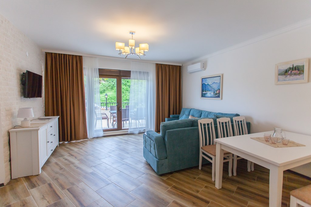 Dnevna soba u stanu u Kamenovu, Crna Gora: plava sofa, trpezarijski deo, izlaz na terasu i svetao enterijer.