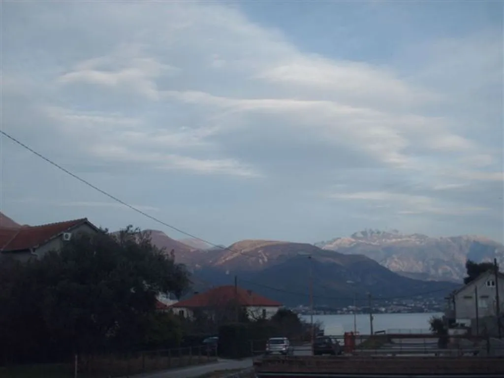 Blick auf Berge und Meer vom Mini-Hotel in Bijela, Montenegro: Panorama mit Häusern, Straße und bewölktem Himmel.