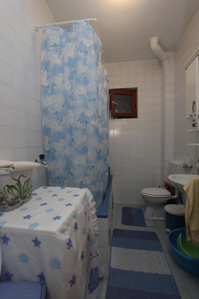 Badezimmer im Haus, Herceg Novi, Montenegro: weiße Fliesen, blaue Duschvorhang mit Delfinen, Sanitäranlagen und Fenster.