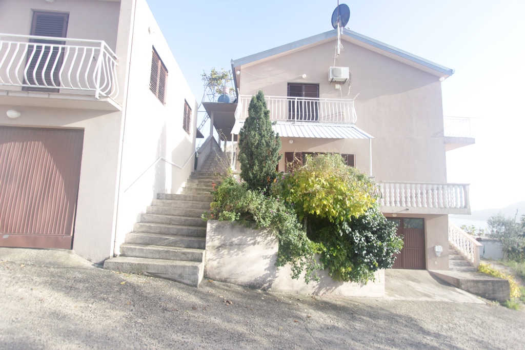 Zweistöckiges Haus mit Garage und Treppe in Herceg Novi, Montenegro, umgeben von Grün und Terrassen mit Balustraden.