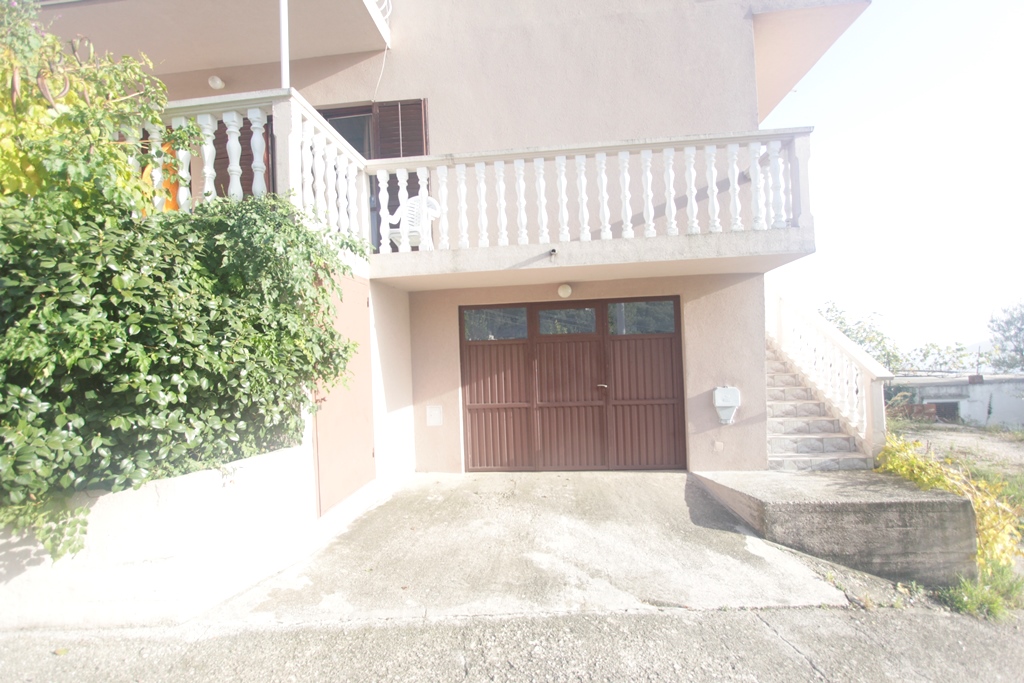 Fassade des Hauses in Herceg Novi, Montenegro: Garage mit braunem Tor, offene Terrasse mit Balustrade und Treppe.
