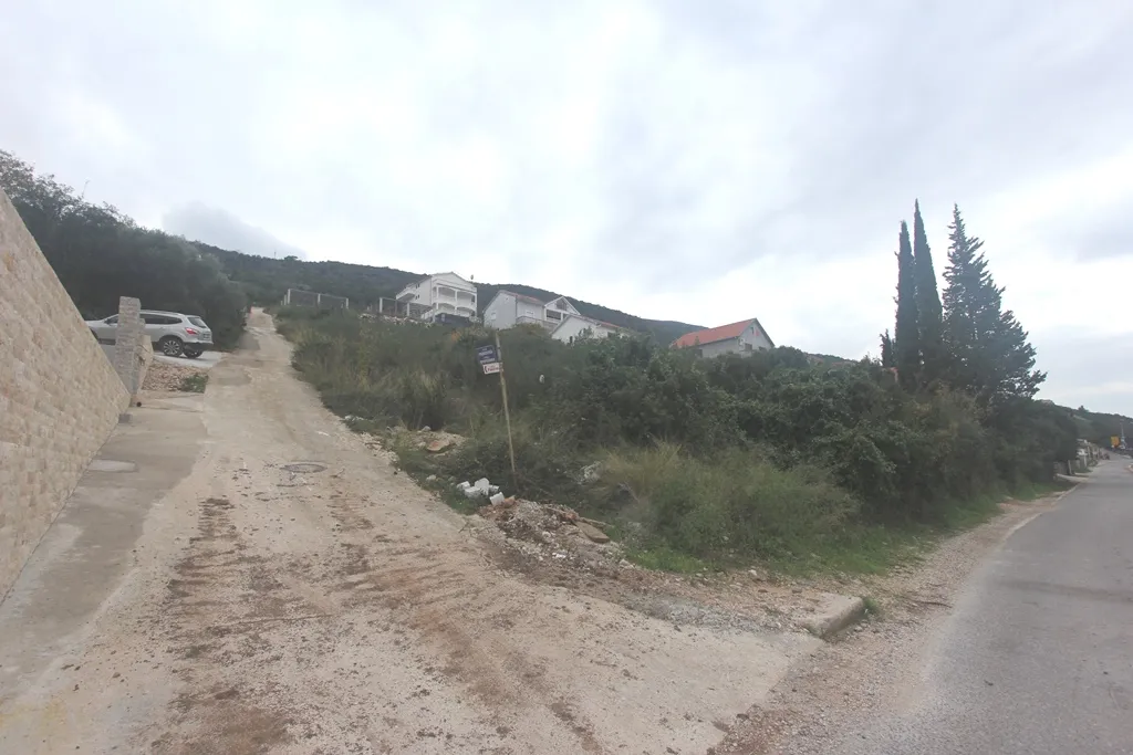 Steep unpaved uphill road leading to residential houses on a hillside under a cloudy sky.