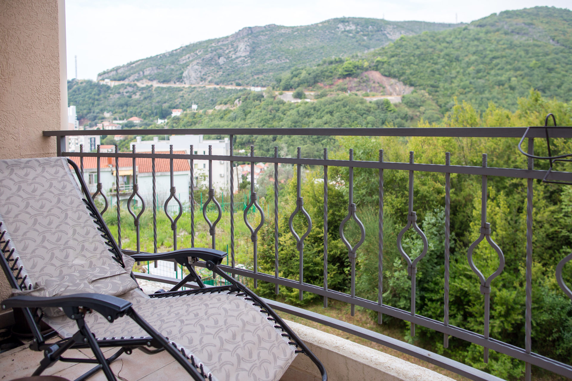 Balkon sa ležaljkom i pogledom na planine i zelenilo u stanu u Bečićima, Crna Gora. Kovano ograda, prijatna terasa.