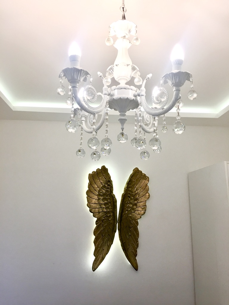 Weißer Kristalllüster und Dekor in Form goldener Flügel im Interieur einer Wohnung in Bečići, Montenegro.