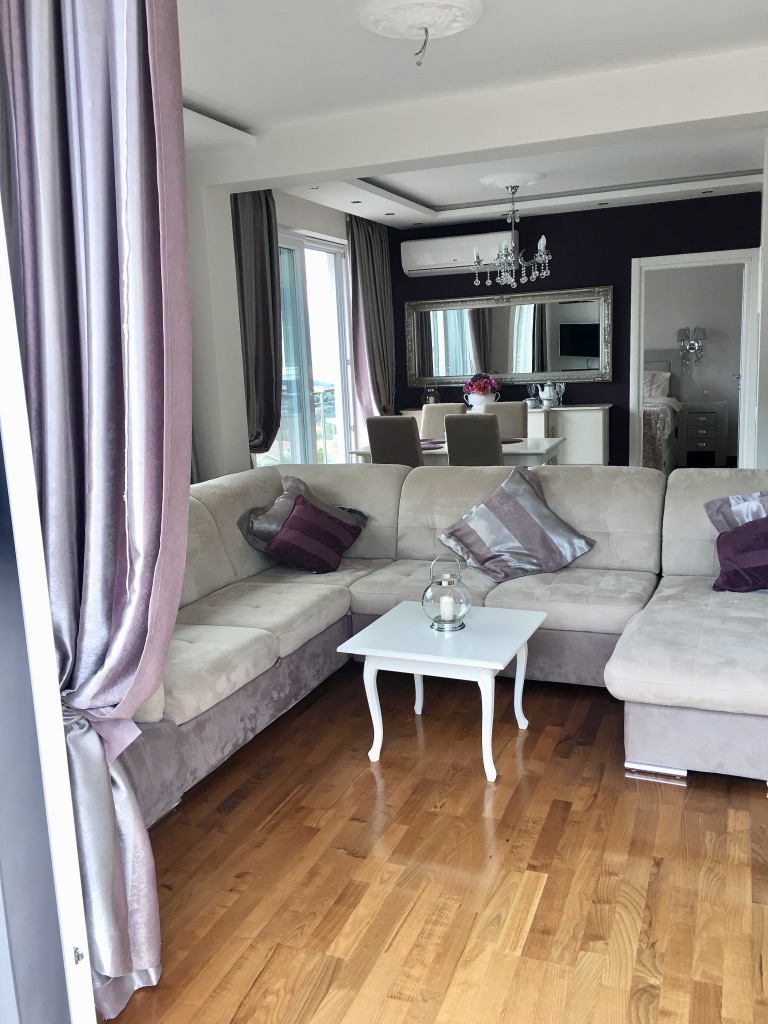Wohnzimmer mit Ecksofa, Essbereich und Parkett in einer Wohnung in Bečići, Montenegro. Modernes Interieur.