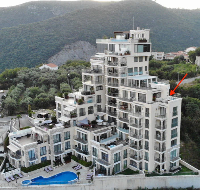 Luftaufnahme eines Wohnkomplexes in Bečići, Montenegro: mehrstöckiges Gebäude mit Terrassen, Pool und Bergen im Hintergrund.