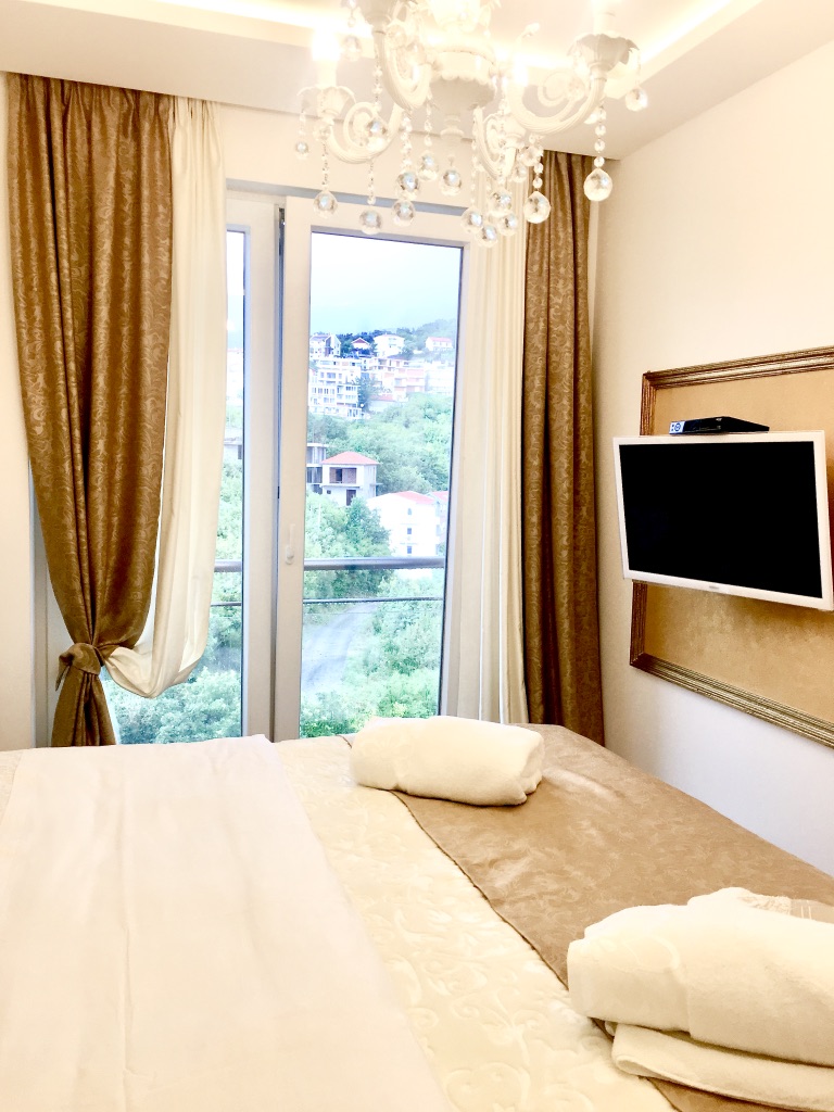 Gemütliches Schlafzimmer in einer Wohnung in Bečići, Montenegro: Doppelbett, TV, Kristalllüster und Bergblick.