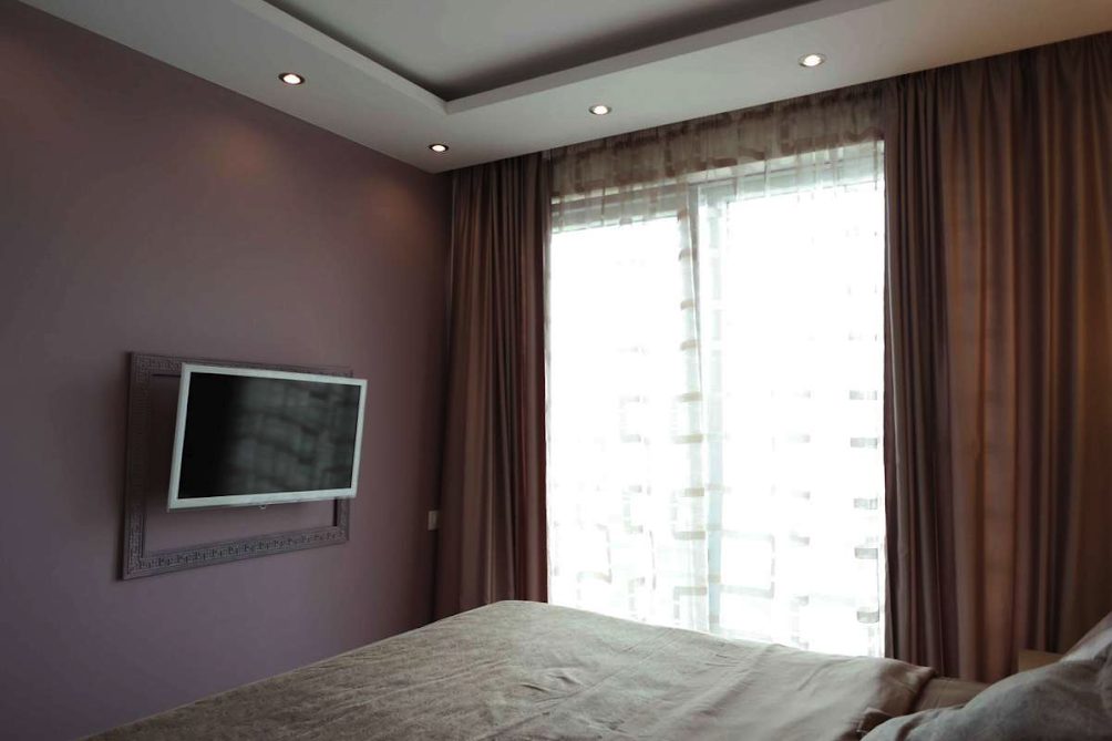 Schlafzimmer in einer Wohnung in Bečići, Montenegro: Doppelbett, TV an der Wand, Panoramafenster mit blickdichten Vorhängen.