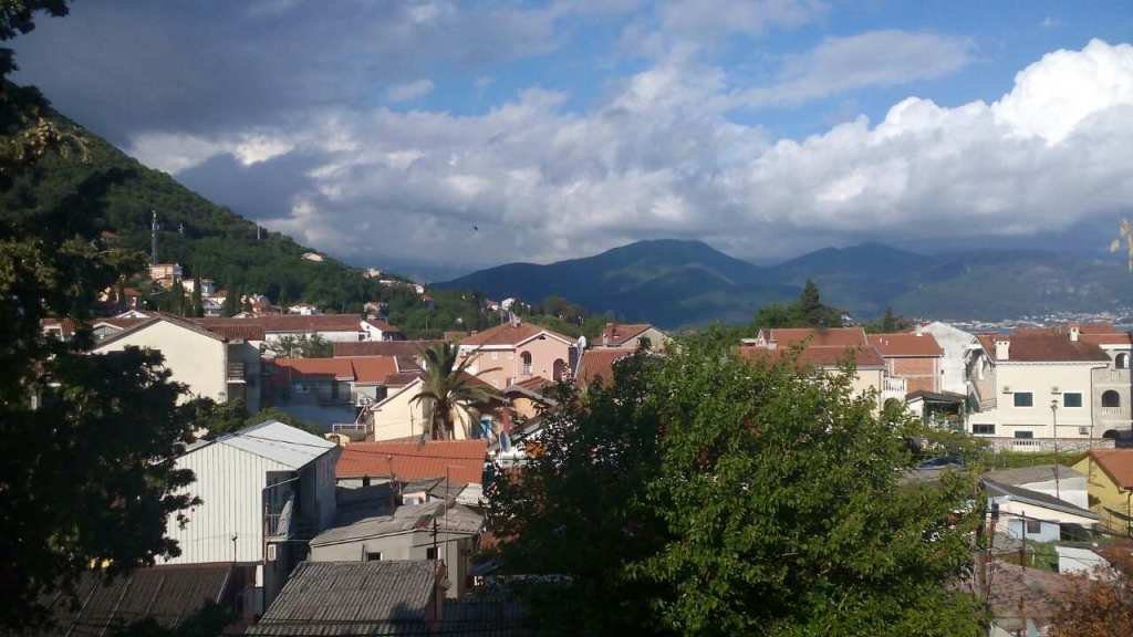 Panoramic view of the mountains and the town of Baošići in Montenegro with tiled rooftops and green trees.