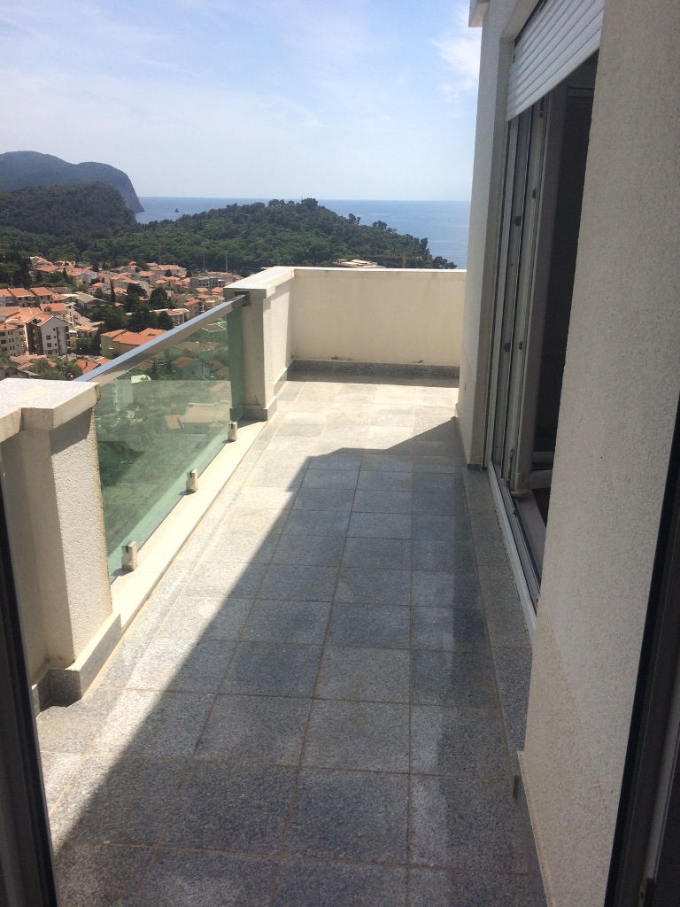 Prostran balkon sa kamenim podom i staklenom ogradom u stanu u Petrovcu, Crna Gora, s pogledom na more.
