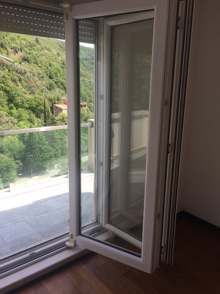 Pogled iz dnevne sobe na terasu i zelene planine u stanu, Petrovac, Crna Gora: panoramski prozori i parket.