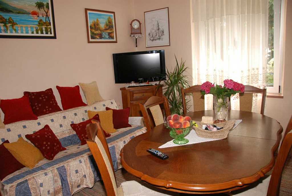 Gemütliches Wohnzimmer in einem Haus in Kamenari, Montenegro: Holzesstisch, weiches Sofa mit Kissen und TV-Bereich.