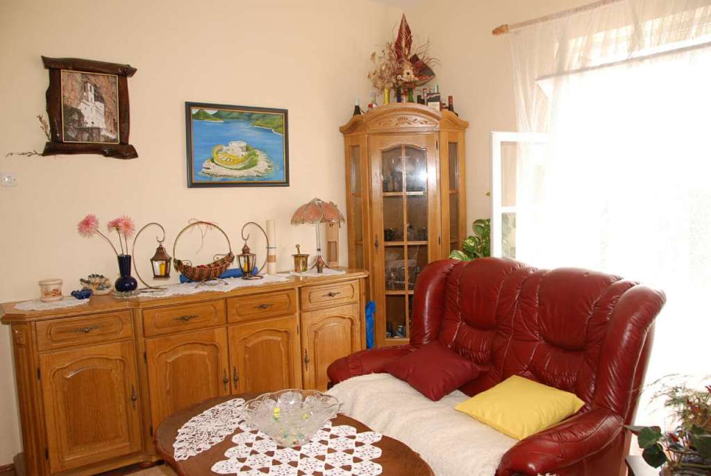 Wohnzimmer in einem Haus in Kamenari, Montenegro: rotes Ledersofa, Holzbuffet, Dekor und helles Fenster.