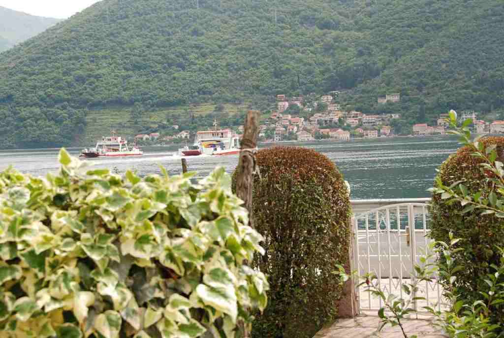 Blick auf die Bucht von Kotor und die Fähre in Kamenari, Montenegro: gepflegter Garten mit Ziersträuchern am Haus.