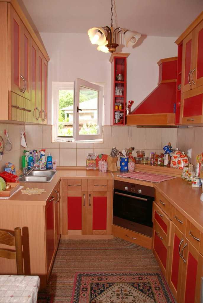 Gemütliche Küche mit roten Fronten in einem Haus in Kamenari, Montenegro: Einbaugeräte, Spüle und Blick aus dem Fenster.