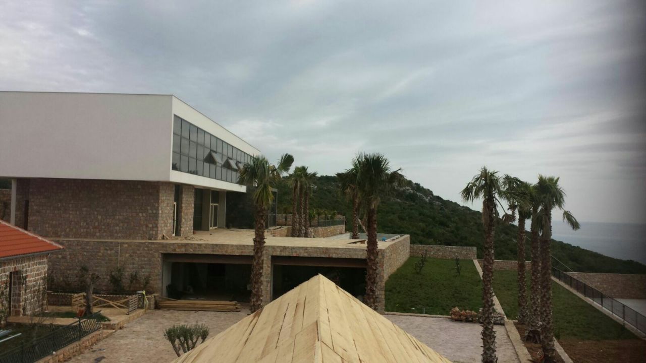 Savremena vila u Krimovici, Crna Gora: kamena fasadna obloga, panoramski prozori i palme u pozadini morskog pejzaža.