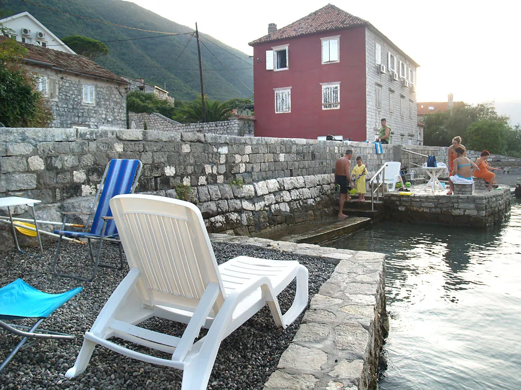 Private beach with sun loungers by a stone villa in Stoliv, Montenegro: sea view and traditional architecture.