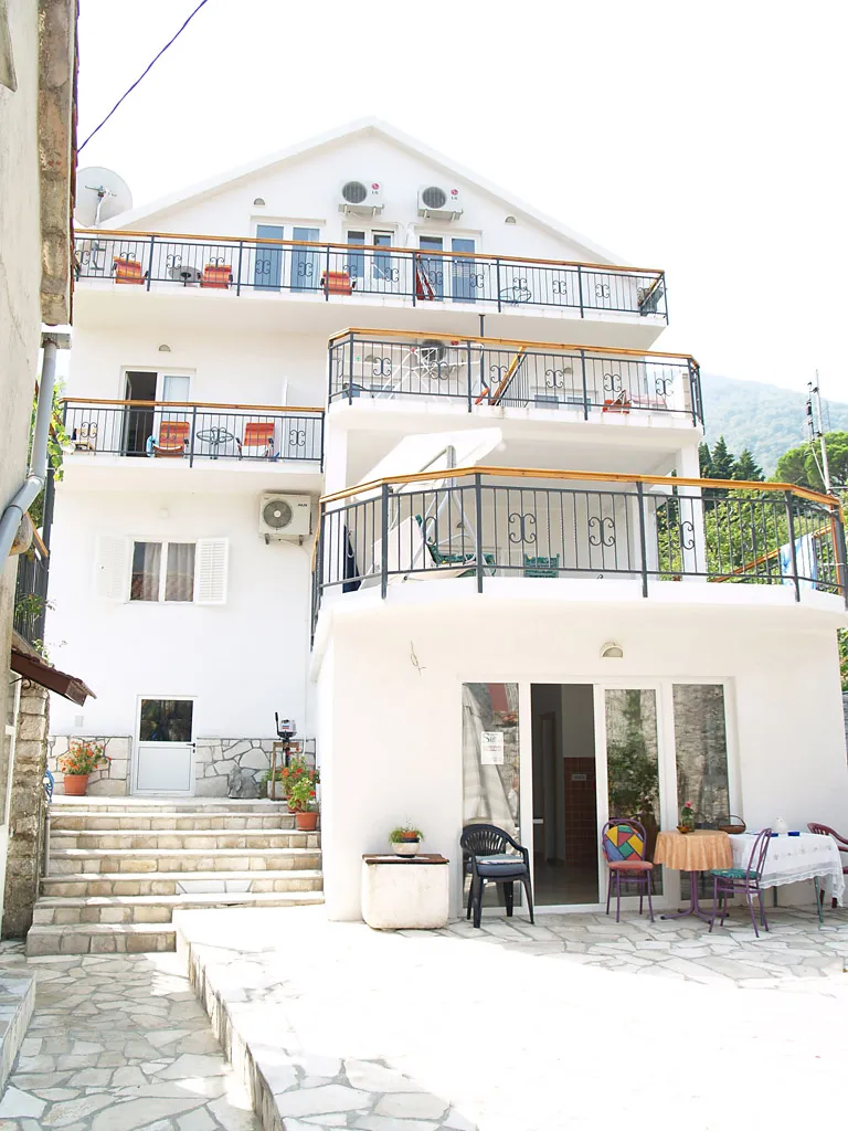 Three-story white villa in Stoliv, Montenegro, with terraces, garden furniture, and stone facade detailing.