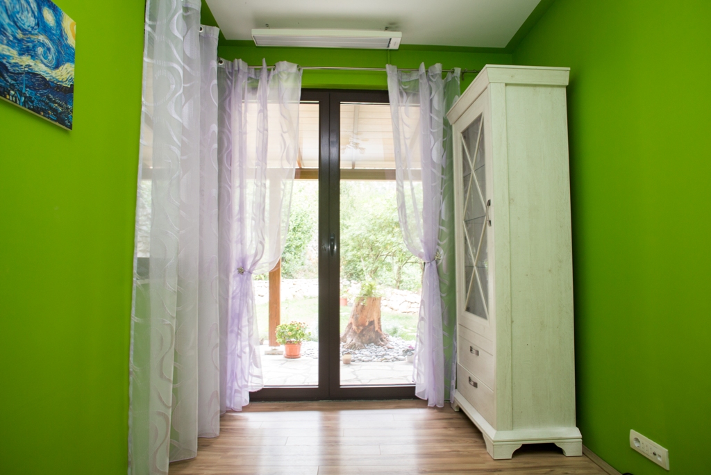 Wohnzimmer in einem Haus in Orahovac, Montenegro: leuchtend grüne Wände, heller Schrank, Panoramatür mit Zugang zur Terrasse.