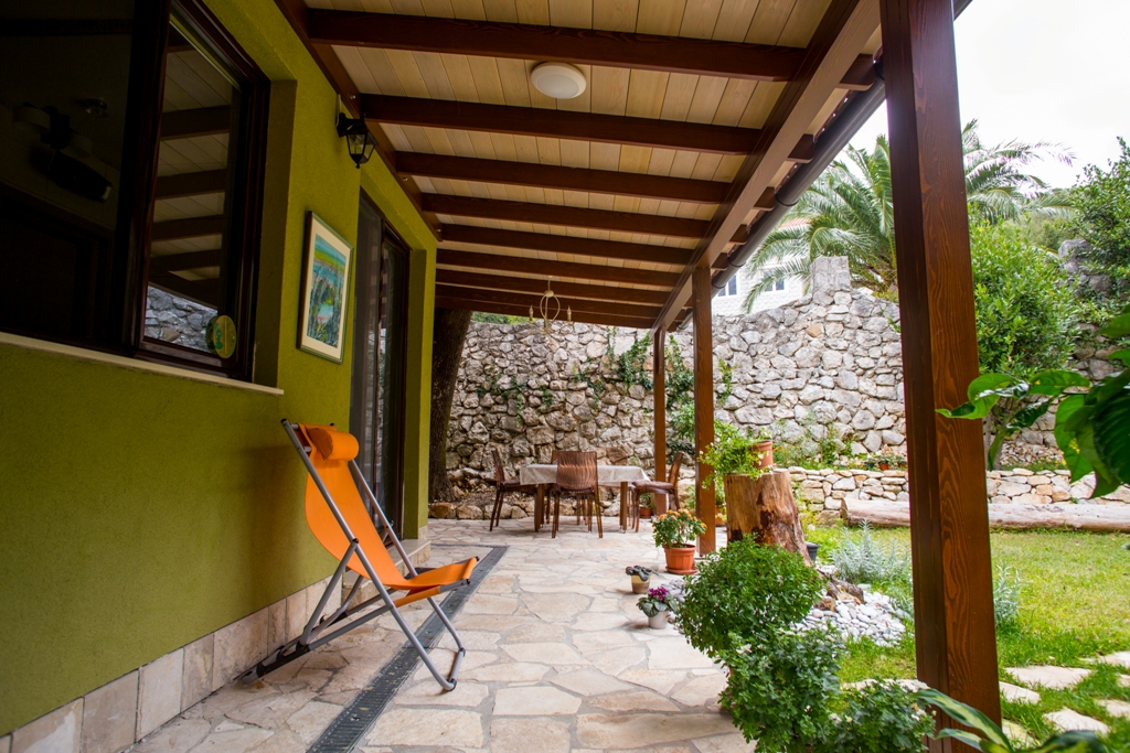 Gemütliche Terrasse eines Hauses in Orahovac, Montenegro: Steinmauerwerk, Holzüberdachung, Möbel und Blick auf den grünen Garten.