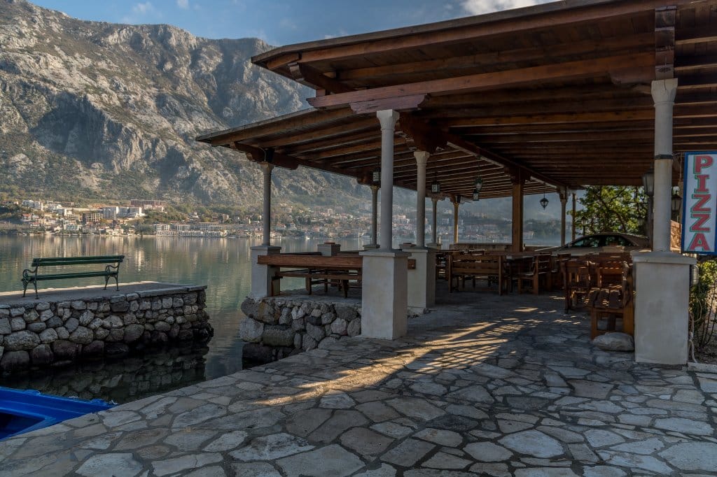 Karadağ, Prčanj’daki villanın terası: taş duvar, ahşap sundurma, Kotor Körfezi ve dağ manzarası.