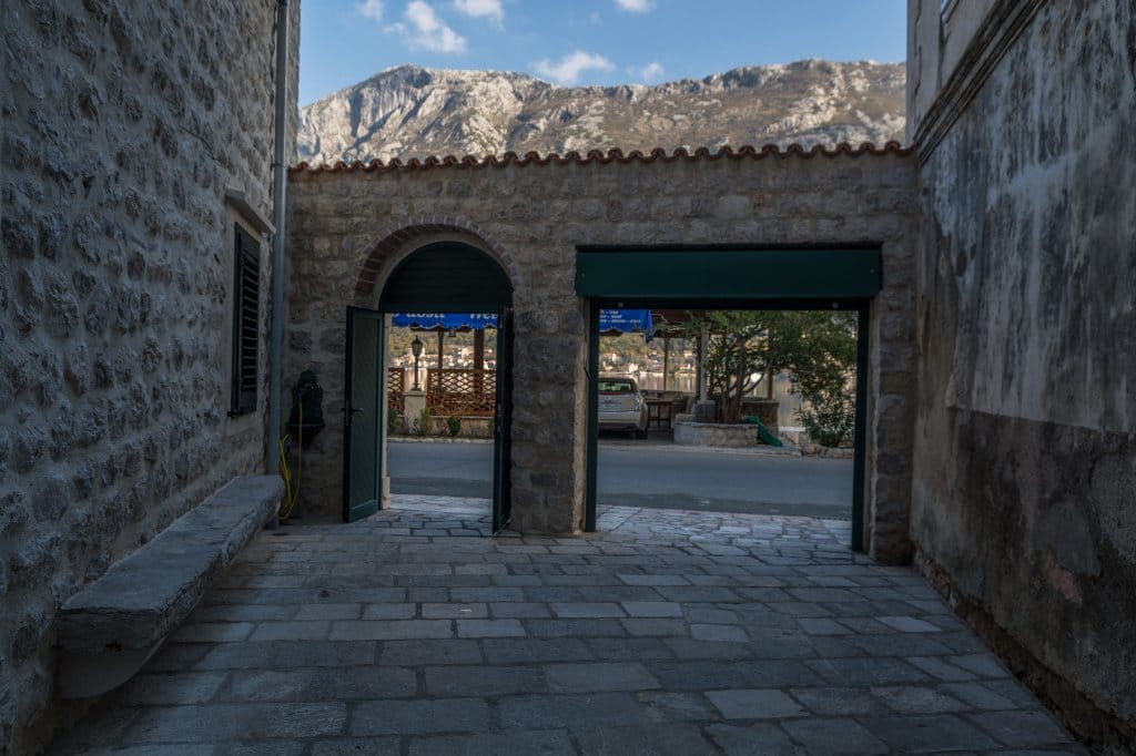 Karadağ, Prčanj’de dağ manzaralı ve sahil yürüyüş yoluna eski bir kemerden çıkışı olan taş villa avlusu.