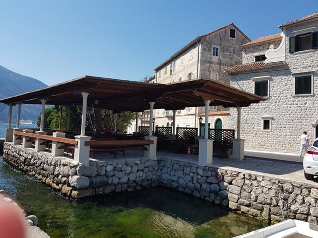 Karadağ, Prčanj’de deniz kenarındaki villanın terası: taş kaplama, ahşap sundurma ve Kotor Körfezi manzarası.