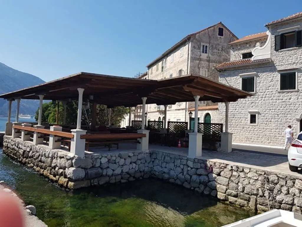 Karadağ, Prčanj’de deniz kenarındaki villanın terası: taş kaplama, ahşap sundurma ve Kotor Körfezi manzarası.