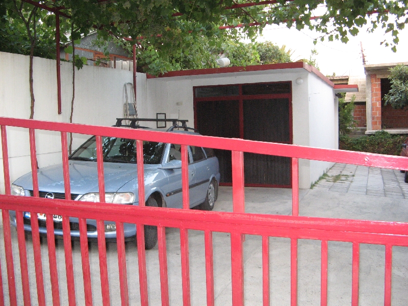Maison privée à Šušanj, Monténégro : garage avec portail rouge, place de parking et vigne dans la cour.