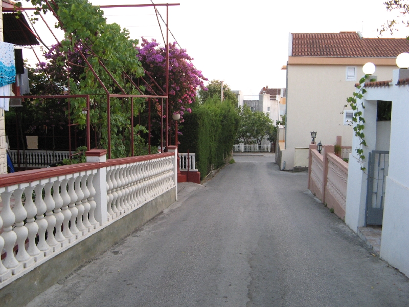 Rue accueillante avec des plantes en fleurs près de la maison à Shushan, Monténégro : vue sur l’allée d’accès et la clôture avec balustrade.