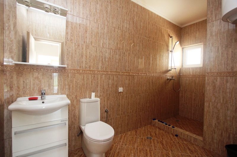 Badezimmer mit Duschkabine und weißer Sanitärkeramik in einem Haus zum Verkauf in Baošići, Montenegro, mit beiger Fliesenverkleidung.