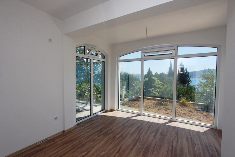 Helles Wohnzimmer mit Panoramafenstern und Meerblick in einem Haus, Baošići, Montenegro. Laminat und weiße Wände.
