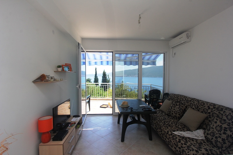 Wohnzimmer mit Zugang zur Terrasse und Meerblick im Haus, Baošići, Montenegro: Sofa, TV-Bereich und Panoramaverglasung.