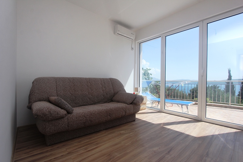 Wohnzimmer in einem Haus in Baošići, Montenegro: Sofa, Panoramafenster mit Meerblick und Zugang zur Terrasse mit Liegestuhl.