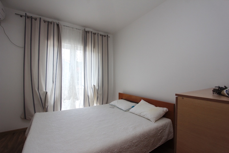 Helles Schlafzimmer mit Doppelbett und Vorhängen in einem Haus in Baošići, Montenegro. Gemütliches Interieur mit Holzmöbeln.