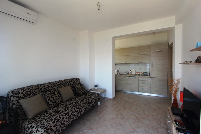 Wohnzimmer mit Küche in einem Haus in Baošići, Montenegro: Sofa mit Blumenmuster, helle Ausstattung und Klimaanlage.